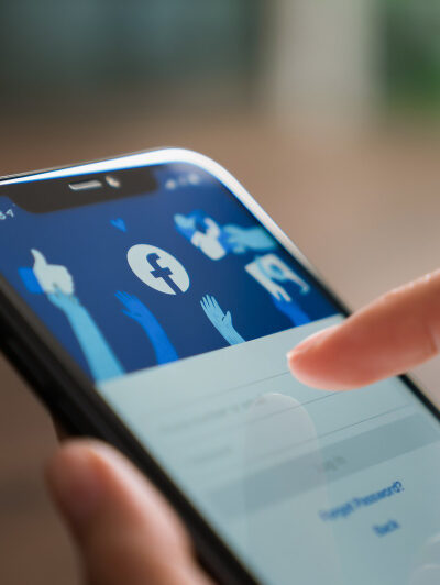 A person's hand is interacting with a smartphone which has a social media application open on the screen, suggesting the use of social networking services.